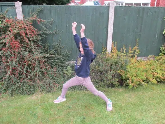 Child doing warrior pose yoga in garden