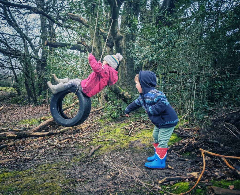 Two children in winter forest pushing each other on a rope swing