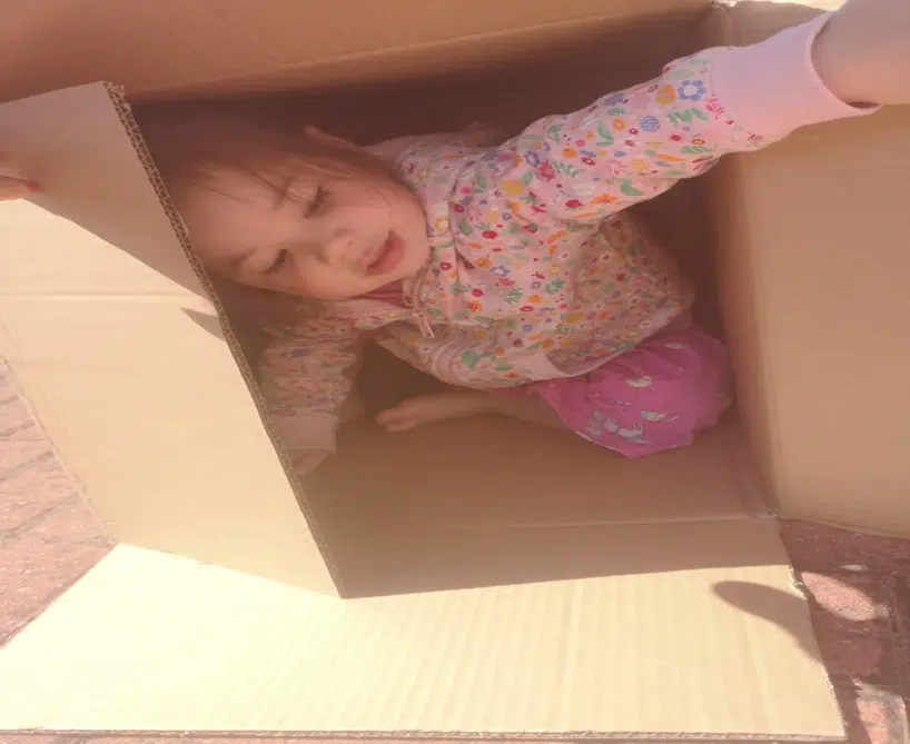 Girl with an enveloping schema hiding in a cardboard box