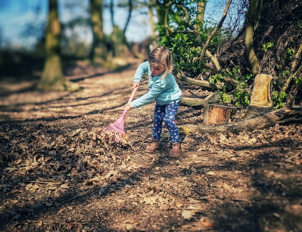 young girl raking leaves in forest school